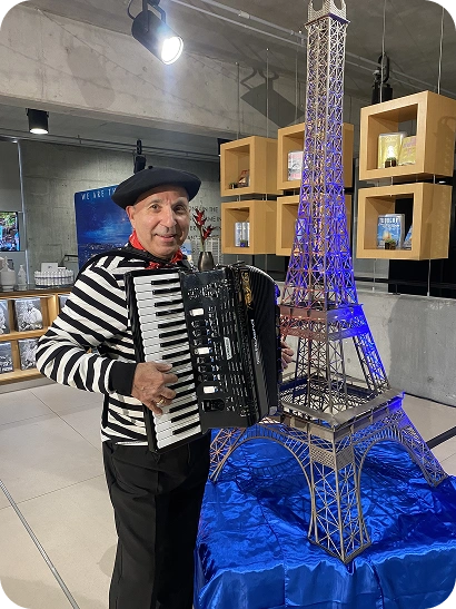 A man dressed in a stylized outfit associated with French culture posing next to a large model of the Eiffel Tower.